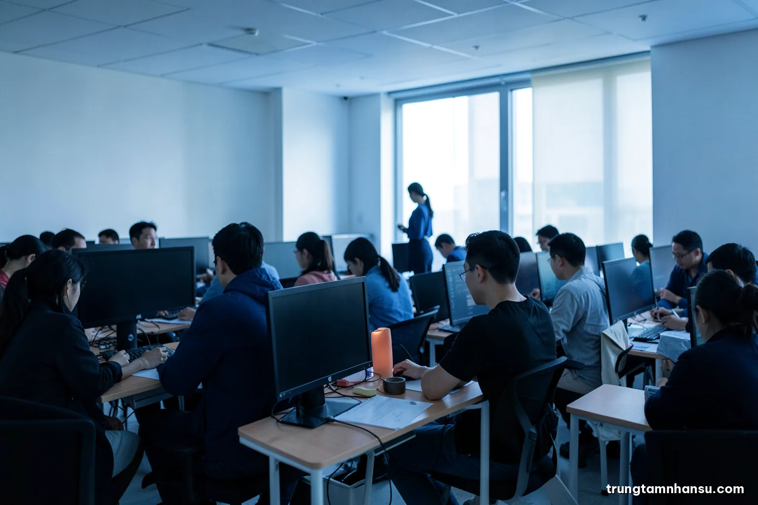 Wide view of a quiet open-plan office at early morning, rows of empty desks with blank monitors, one person in silhouette by the window, cool blue light, minimal composition