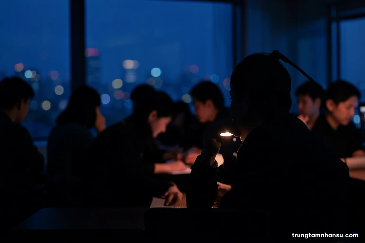 Silhouette of a person sitting alone at a desk late at night in a dim office, head resting on one hand, single desk lamp glow, city lights blurred behind, deep indigo palette