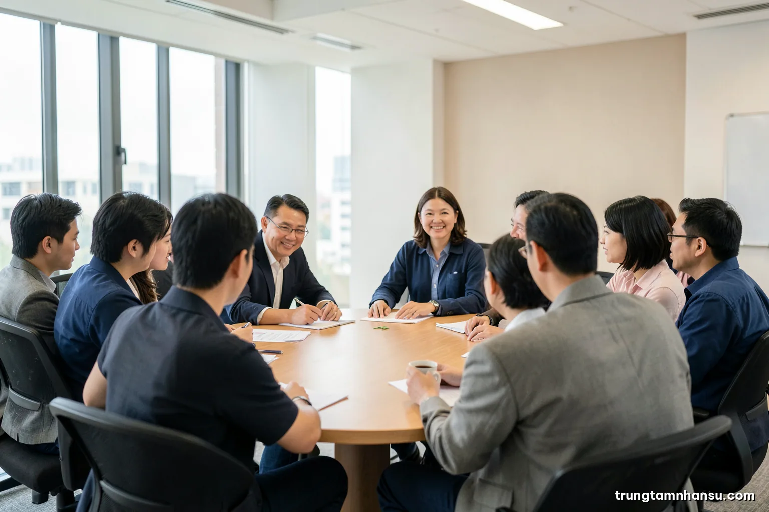 Wide shot of a modern Vietnamese office meeting with a foreign manager and local staff around an oval table, everyone seen from behind or side, soft overcast light, beige and navy palette