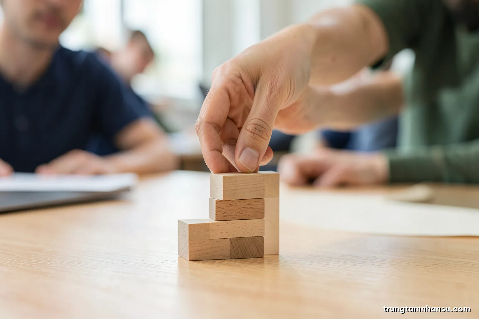 Macro shot of a hand placing small wooden blocks into three ascending stacks on a light oak desk, minimalist composition, diffused window light, beige and sage green palette